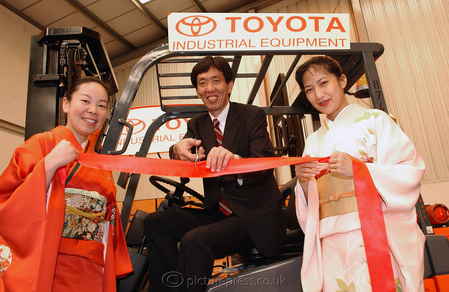 opening of toyota facility in birmingham. managing director with 2 ladies in tradional costume cutting ribbon on fork lift truck.  image produced for a news release. taken  by mike kelly  photographer picturepress.